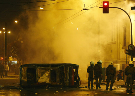 Policemen take cover behind a burnt car during riots in Athens December 7, 2008. 
