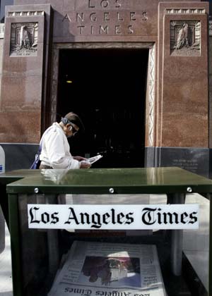 A man stands between a 'Los Angeles Times' newspaper vending machine and an entrance to the Times building in downtown Los Angeles April 2, 2007. Faced with a mountain of debt and shrinking advertising revenue, the Chicago-based Tribune Co., which owns the Los Angeles Times, filed for Chapter 11 bankruptcy protection on Monday. [Xinhua/Reuters]