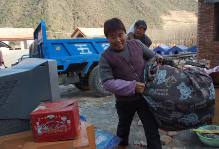 Photo dated on Dec. 8, 2008 shows villagers carry their belongs at the relocated Quanli village in Lueyang county, northwest China's Shaanxi Province. Two hundred and six quake-survived villagers have moved into their new houses in the newly-built village prior to the upcoming winter.(Xinhua Photo)