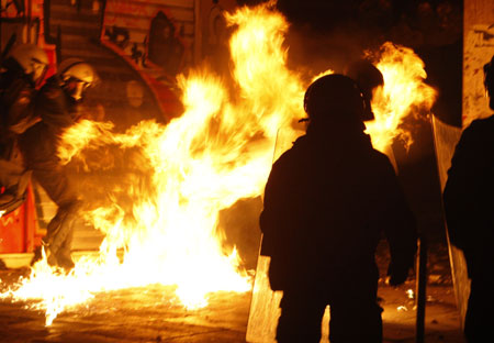 Policemen protect themselves from a Molotov cocktail during riots in Athens, December 8, 2008. Thousands of protestors rampaged through the heart of Athens on Monday, burning and looting shops on a third day of riots sparked by the killing of a teenager by police. [Agencies via China Daily]