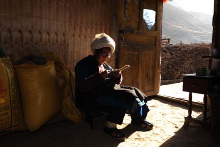 Wang Taozhi, 68, sews an insole as she sits beside the bags of food that distributed by the local government, in Luobozhai Village of Yanmen Township, the quake-hit Wenchuan County, southwest China's Sichuan Province, Dec. 8, 2008.