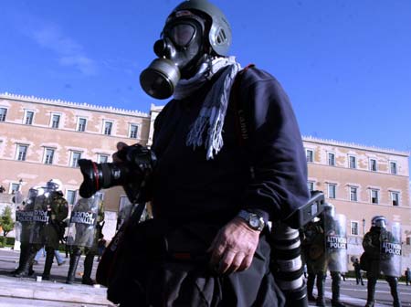 A photographer wearing a gas mask walks past the Greek Parliament during a protest march in Athens, capital of Greece, Dec. 12, 2008. Riot police on Friday clashed with youths on the seventh day of Athens riots triggered by the death of the 15-year-old boy last Saturday. (Xinhua/Yang Shaobo)