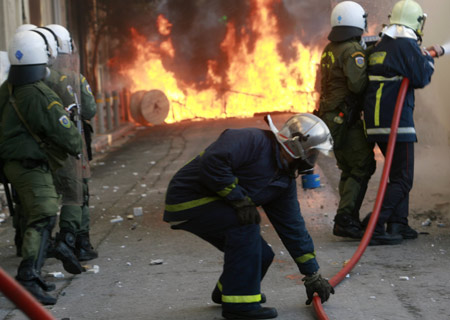 Firefighters and riot policemen extinguish a fire on a burning van outside Athens' Law school during riots December 18, 2008.