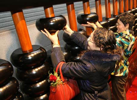 Visitors try to lift the beads of the huge abacus, one of which weighs 6.3 kilograms, at China Abacuses Museum in Nantong, east China's Jiangsu Province, Dec. 20, 2008. The abacus, 781 centimeters in length and 1.81 centimeters in height, has been on display here since Saturday. 