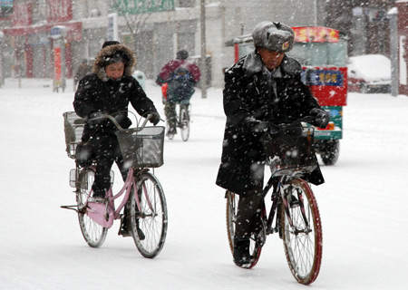 People ride bicycle on a snow-covered road in Tianjin, north China, Dec. 21, 2008. 
