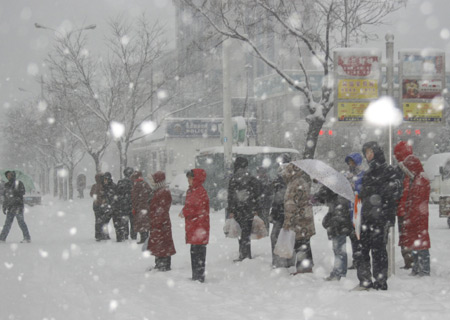 People wait for buses on a snow-covered road in Penglai of Yantai city, east China's Shandong Province, Dec. 21, 2008. A strong cold front hit Yantai on Sunday, causing a snowfall and sharply bringing down the temperature. 