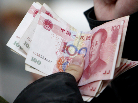 A customer holds renminbi banknotes at an ATM in a bank in Beijing, Nov 26, 2008.The yuan will be used in transactions with neighboring trade partners as part of a pilot project - in what could be the first step on the road to making it an international currency. [Xinhua]