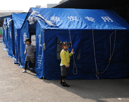 Two girls play outside makeshift houses in Ruili of Southwest China's Yunnan Province aftert three earthquakes measuring 4.9, 4.3 and 4.0 on the Richter scale hit Southwest China on December 26, 2008. The earthquakes have left 19 wounded and 49,789 affected. [Xinhua] 