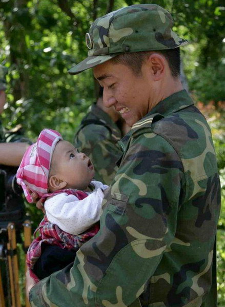 A loyal solider and an innocent child stare at each other. The solider took the baby from its grandmother while walking across a bridge on the afternoon of May 14. He carried the child for 1.5 kilometers to safety. The May 12 earthquake caused heavy casualties and inflicted psychological trauma on numerous victims. [People&apos;s Daily]