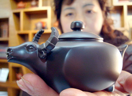 A saleswoman shows a teapot made of purple sand with an ox head-shaped spout, at a shop in Suzhou, east China's Jiangsu Province, Dec. 31, 2008. As the Chinese Year of Ox, the lunar New Year, draws near, teapots decorated with the image of oxen are sold well. The Chinese New Year starts from Jan. 26 according to the traditional lunar calendar. [Xinhua] 