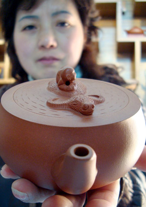 A saleswoman shows a purple sand teapot with its lid decorated with the image of ox, at a shop in Suzhou, east China's Jiangsu Province, Dec. 31, 2008. [Xinhua]