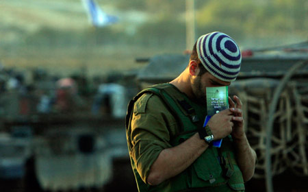 An Israeli soldier prays beside the tanks in the Gaza Strip Jan. 6, 2009. The Israeli army has said that it would hold fire in the Gaza Strip for three hours every day from Jan. 7 to allow local residents to prepare basic supplies. [Tsafrir Abayov/Xinhua] 