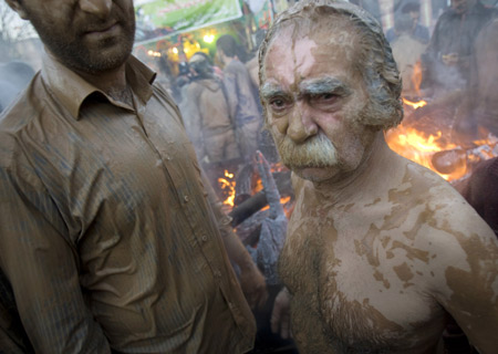 An Iranian man covered in mud stands near a fire to dry himself during the Ashura religious festival in Khorramabad, 491 km (307 miles) southwest of Tehran, Jan. 7, 2009. [Xinhua]