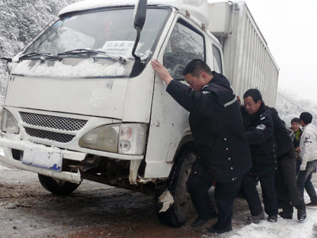 Policemen and passengers push a truck on a frozen slope in Tujia-Miao Autonomous County of Yinjiang, southwest China's Guizhou province, Jan. 7, 2009. Due to the flow of strong cold air, many regions of Guizhou Province were hit by freezing rain and sleet recently. Workers of road administrative department started to scatter skidproof sands on the frozen road in Tongren area.[Chen Xiaolan/Xinhua]