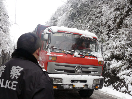 A truck passes a part of a frozen road under the guide of a policeman in Tujia-Miao Autonomous County of Yinjiang, southwest China's Guizhou province, Jan. 7, 2009. Due to the flow of strong cold air, many regions of Guizhou Province were hit by freezing rain and sleet recently. Workers of road administrative department started to scatter skidproof sands on the frozen road in Tongren area.[Chen Xiaolan/Xinhua] 