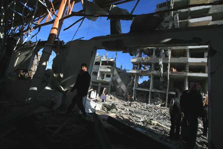 Palestinians walk past a building destroyed by Israeli strikes in Gaza City on Jan. 13, 2009. Israeli soldiers fought heavy battles with local militants in Gaza early Tuesday. Medics said Monday that over 900 people have been killed and more than 4,100 others wounded since Israeli military operation on Dec. 27, 2008. [Wissam Nassar/Xinhua]