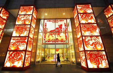 A pedestrian passes the door of a shopping mall decorated with the paper-cut work with the theme of the Year of Ox on the Nanjing Road in Shanghai, China, Jan. 13, 2009. As the Year of Ox in Chinese lunar calendar approaching, the city is permeated with a holiday atmosphere. The Chinese Year of Ox will start from Jan. 26, 2009. [Xinhua]