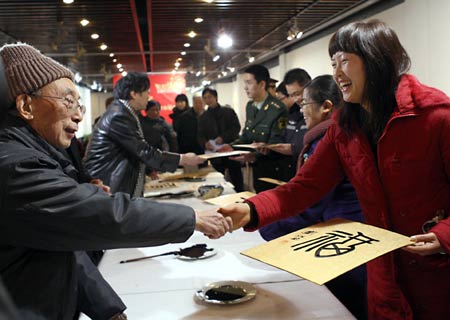 Liu Jiangshu (L), professor of China Academy of Art, presents his work of 'fu', meaning 'good wishes', to a woman during a calligraphy activity held in Hangzhou, capital of east China's Zhejiang Province, Jan. 15, 2009, to greet the Chinese lunar New Year starting from Jan. 26. [Cheng Ruixin/Xinhua]
