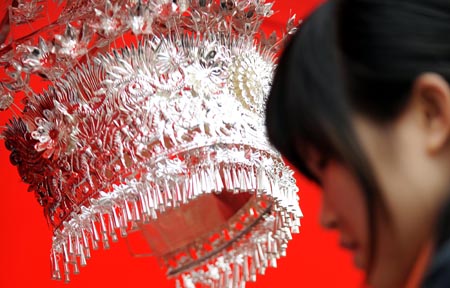 A visitor stands in front of the fengguan, a silver hair decoration for females of Chinese Miao ethnic group, during a fair of the intangible cultural heritage, in Changsha, capital of central China's Hunan Province, Jan. 17, 2009.