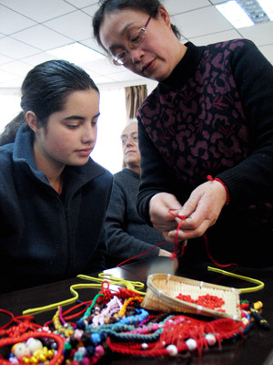 Hu Lihua (R), a folk artisan, shows the skill of weaving Chinese knots to a New Zealand student in Shandong Normal University in Jinan, capital of east China's Shandong Province, Jan. 19, 2009. [Xinhua]