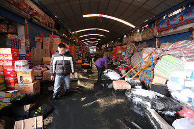 Vendors clean up a wholesale market that was flooded by river sludge on Zhenda Road in Dachang Town Monday. The silt, waste from a dredging project, was being stored behind a wall at a former marble factory. The wall's collapse caused a wave of black water to hit the market. [Zhao Yun/Shanghai Daily]