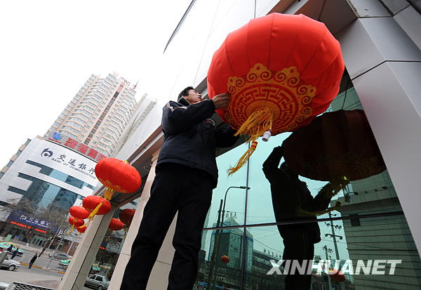 A man hangs up red lanterns on a downtown office building in Lanzhou, capital city of northwest China's Gansu province on Monday, January 19, 2009. [Photo: Xinhuanet]