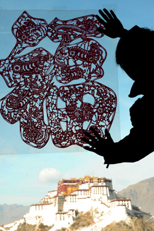 A man sticks a paper-cut of Chinese character of 'Fu', meaning 'good fortune', onto the window at a cafe to celebrate the Spring Festival in Lhasa, capital of southwest China's Tibet Autonomous Region, Jan. 25, 2009. [Xinhua]