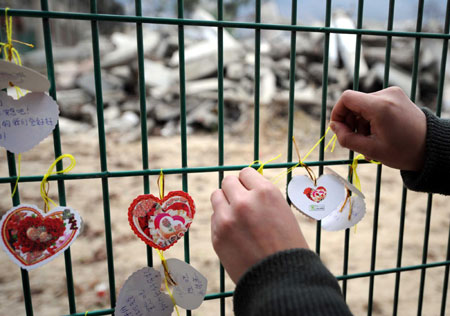 A woman ties a heart-shaped card with condolences to quake victims to rails enclosing the ruins of Beichuan Middle School in Sichuan province January 25, 2009, the Chinese Lunar New Year Eve. [Xinhua]