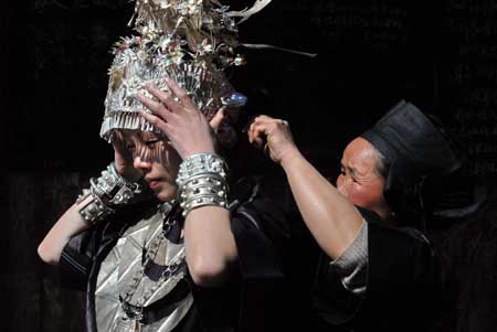 A girl of Miao ethnic group puts on her headwear with the help of an old woman in the Zhanliu Village of Jianhe County, southwest China's Guizhou Province, Jan. 31, 2009. It was the second day of the traditonal Embroidery Sisters Festival, which falls on the fifth to the seventh day of the first month in Chinese Lunar calendar. Villagers worshiped ancestor, performed Lusheng (the ethnic emblematic reed-pipe blowing instrument) and held gala during the festival. [Qiao Qiming/Xinhua] 