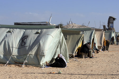 Palestinians who lost their home during the 22-day Israeli offensive sit by tents at a refugee camp in Jabalia, northern Gaza Strip, Jan. 31, 2009. (Xinhua/Wissam Nassar)