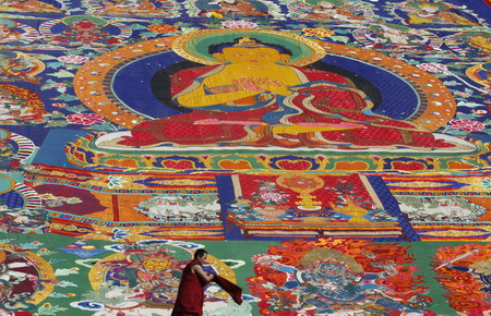An ethnic Tibetan monk walks in front of a giant 'thangka', a sacred painting on cloth, to be displayed on a hill outside a monastery in Tongren, northwest China's Qinghai province Monday, Feb. 2, 2009. (Photo: China Daily) 
