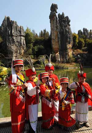 Kids dressed in local ethnic costumes pose for a group photo in front of the Stone Forest near Kunming, capital of southwest China's Yunnan Province, Feb. 4, 2009. Spring comes to southwest China's Yunnan province. (Xinhua/Lin Yiguang)