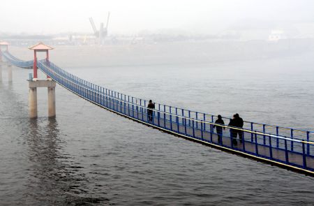 Tourists walk on an iron-chain bridge near the outlet of the Xiaolangdi Dam on the Yellow River in central China's Henan Province, Feb. 5, 2009. The Yellow River Flood Control and Drought Relief Headquarters has launched an orange alert for grim drought situation on Tuesday. The daily average water flow through the Xiaolangdi Dam was increased to 600 cubic meters per second to help soothe the drought in areas along the Yellow River. [Miao Qiunao/Xinhua]