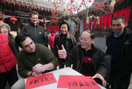 A U.S. citizen (L) learns the brush calligraphy of Chinese characters, literally, 'Happy Lantern Festival', during a get-together party of local residents and foreigners living on Dongsisitiao Hutong (Alley), inside a quadrangle courtyard, the typical residential rectangular compound, to live a jovial Chinese lunar Lantern Festival, in Beijing, Feb. 8, 2009. [Hao Fei/Xinhua]