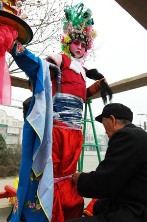 A teenager performer is being garbed as one of the popular theatric or legendary figures, to be towering high on the floral sedans during a local folklore Xin Zi promenade for the lantern festival jollification, on the avenue of Zhoucun District, Zibo City, east China's Shandong Province, Feb. 8, 2009.(Xinhua/Dong Naide) 