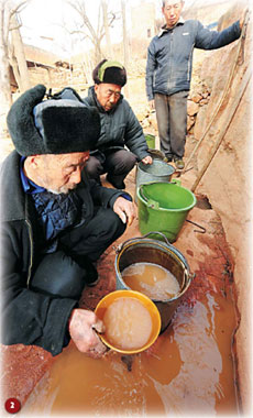Xue Yongguo (left), a 79-year-old villager in Zhanghe, Henan province, ladles out muddy water to drink last week at the foot of a nearby mountain. The closest alternative for drinking water is two hours away on foot. [Gao Shanyue/China Daily] 