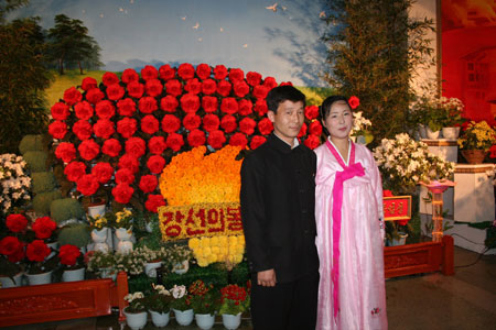 A couple pose for photos at an exhibition on 'Kim Jong Il flowers' held in Pyongyang, capital of the Democratic People's Republic of Korea (DPRK), Feb. 14, 2009. The exhibition was held to celebrate the upcoming 67th birthday of DPRK top leader Kim Jong Il. [Xinhua]