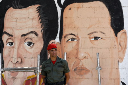 A Presidential honor guard stand next to a mural of Venezuelan President Hugo Chavez (R) and national hero Simon Bolivar outside a polling station in Caracas February 15, 2009. Venezuelans voted on Sunday on a proposal that would allow Chavez to stay in power for as long as he keeps winning elections. [China Daily/Agencies]