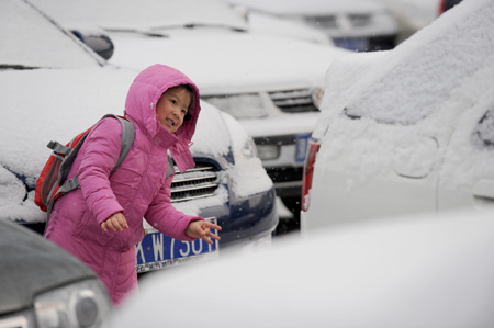 A girl walks past cars covered with snow in a parking lot in Beijing's Shijingshan district yesterday. The city experienced its first snow this winter yesterday, though the suburbs received some snowfall on Dec 10 and 23. [Xinhua]