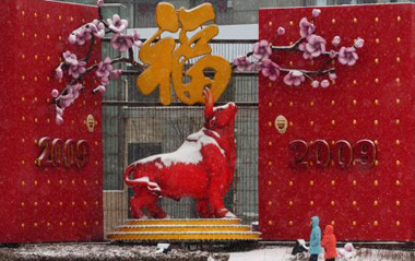 Two Chinese walk past an ox statue during a snowfall in the costal city of Dalian, northeast China's Liaoning Province, Feb. 18, 2009. Rain and snowfall have helped ease a severe drought in northern and eastern China. [Lv Wenzheng/Xinhua]