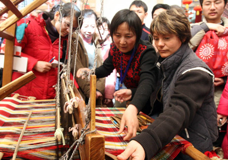 A foreigner learns the skills of knitting brocade cloth from Liu Aiyu (2nd, R), a folk heir in brocade knitting from east China's Shandong Province, at an exhibit of China's intangible cultural heritage in Beijing, China, Feb. 22, 2009. Many visitors have been attracted to learn and practise traditional crafts while visiting the exhibition, which was held here from Feb. 9 to Feb. 23.[Chen Xiaogen/Xinhua] 