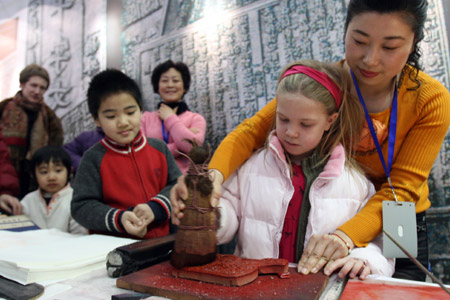 An employee helps a foreign girl make print with an engraved block at an exhibition of of China's intangible cultural heritage in Beijing, China, Feb. 22, 2009.[Chen Xiaogen/Xinhua]