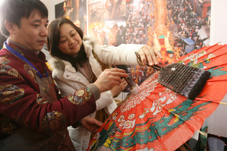 Xu Xueming (L), a folk artist, teaches a visitor skills in making umbrella at an exhibition of of China's intangible cultural heritage in Beijing, China, Feb. 22, 2009.[Chen Xiaogen/Xinhua] 