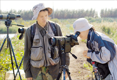 Two Shanghai Wild Bird Society members watch birds through binoculars on Chongming Island. [Shanghai Daily] 