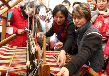 A foreigner learns the skills of knitting brocade cloth from Liu Aiyu (2nd, R), a folk heir in brocade knitting from east China&apos;s Shandong Province, at an exhibit of China&apos;s intangible cultural heritage in Beijing, China, Feb. 22, 2009. Many visitors have been attracted to learn and practise traditional crafts while visiting the exhibition, which was held here from Feb. 9 to Feb. 23.(Xinhua/Chen Xiaogen)
