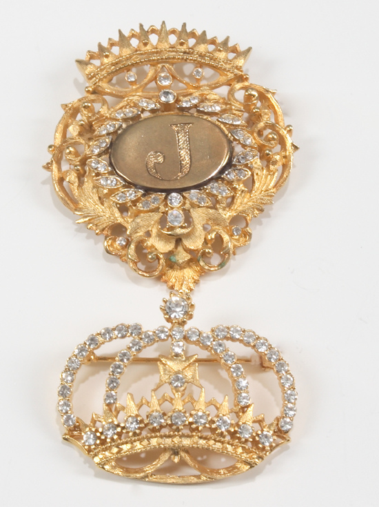 A gold metal brooch with elaborate foliate design topped with crown motif framing a central oval cartouche with the letter 'J' together with a matching brooch in the form of a crown set with rhinestones. Estimate: $150 - $200 [China.org.cn/Julien's Auctions/Shaan Kokin] 