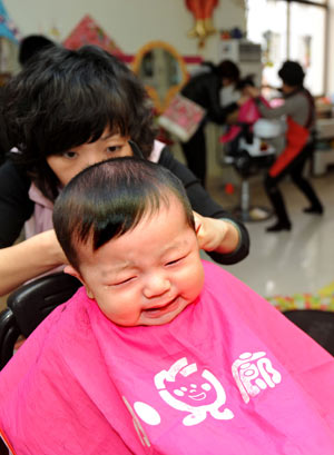 A hairdresser cuts hair for a child at a children hairdressing shop in Qingdao, east China's Shandong Province, Feb. 26, 2009. The day is the second day of the second month according to the lunar calender. It is believed in China that cutting hair on the day will bring good luck.