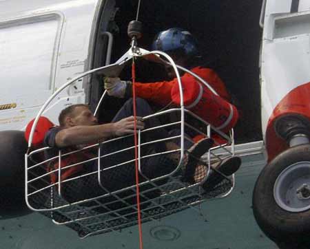 A U.S. Coast Guard helicopter crew member (R) reaches out to pull a man, identified by the Coast Guard as Nick Schuyler, from a transport basket into the helicopter after the man was rescued from the waters of the Gulf of Mexico, off the coast of St. Petersburg, Florida March 2, 2009.