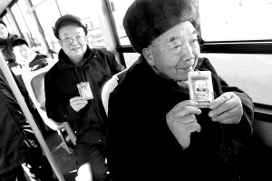 The photo taken on January 1, 2009 shows two old men taking bus with their coutresy cards. From 2009, Beijing seniors over age 65 are able to take buses, visit parks, and go sightseeing for free with a kind of courtesy card. However, non-local seniors have to pay the fares and tickets on their own. [File Photo: Beijing Morning Post]