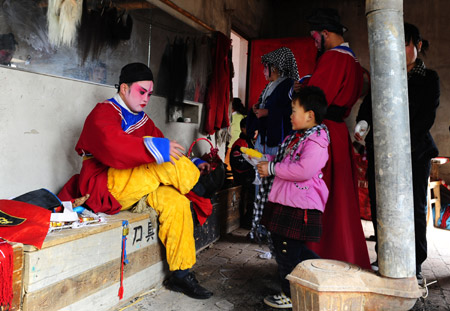 A child looks at the performer as he changes costumes at Halagui Village in Chaoyang County, northeast China's Liaoning Village, March 15, 2009.[Ren Yong/Xinhua]